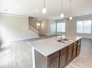 a kitchen and living room with a staircase in the background